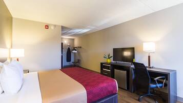 A hotel room with a bed, desk, chair, television, and a small kitchenette.