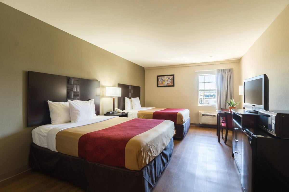 A hotel room with two beds, a desk, a television, and a window with curtains.