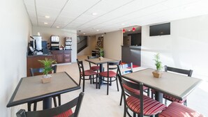 A modern dining area with multiple tables and chairs, a kitchen area in the background, and a staircase leading to another floor. - Econo Lodge Harrisburg - Southwest of Hershey Area (Harrisburg)