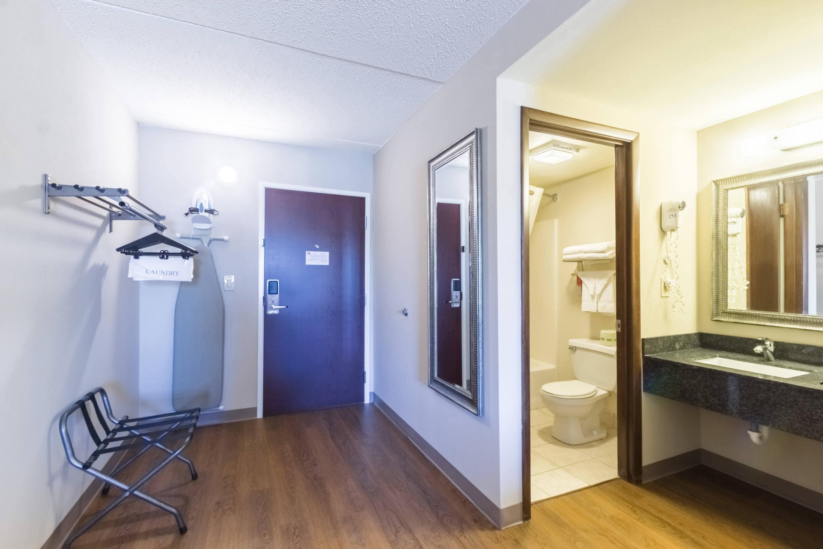 Une chambre d’hôtel avec un plancher en bois, un grand miroir, un lavabo et une porte donnant sur une salle de bain.