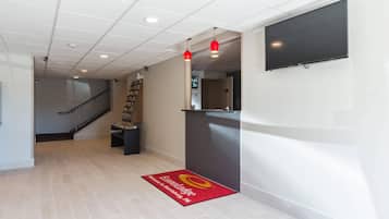Un vestíbulo de hotel con piso de baldosas, mostrador de recepción, escalera y televisor de pantalla plana montado en la pared.
