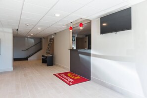 Un hall d’hôtel avec un sol carrelé, un comptoir d’accueil, un escalier et un téléviseur à écran plat fixé au mur.