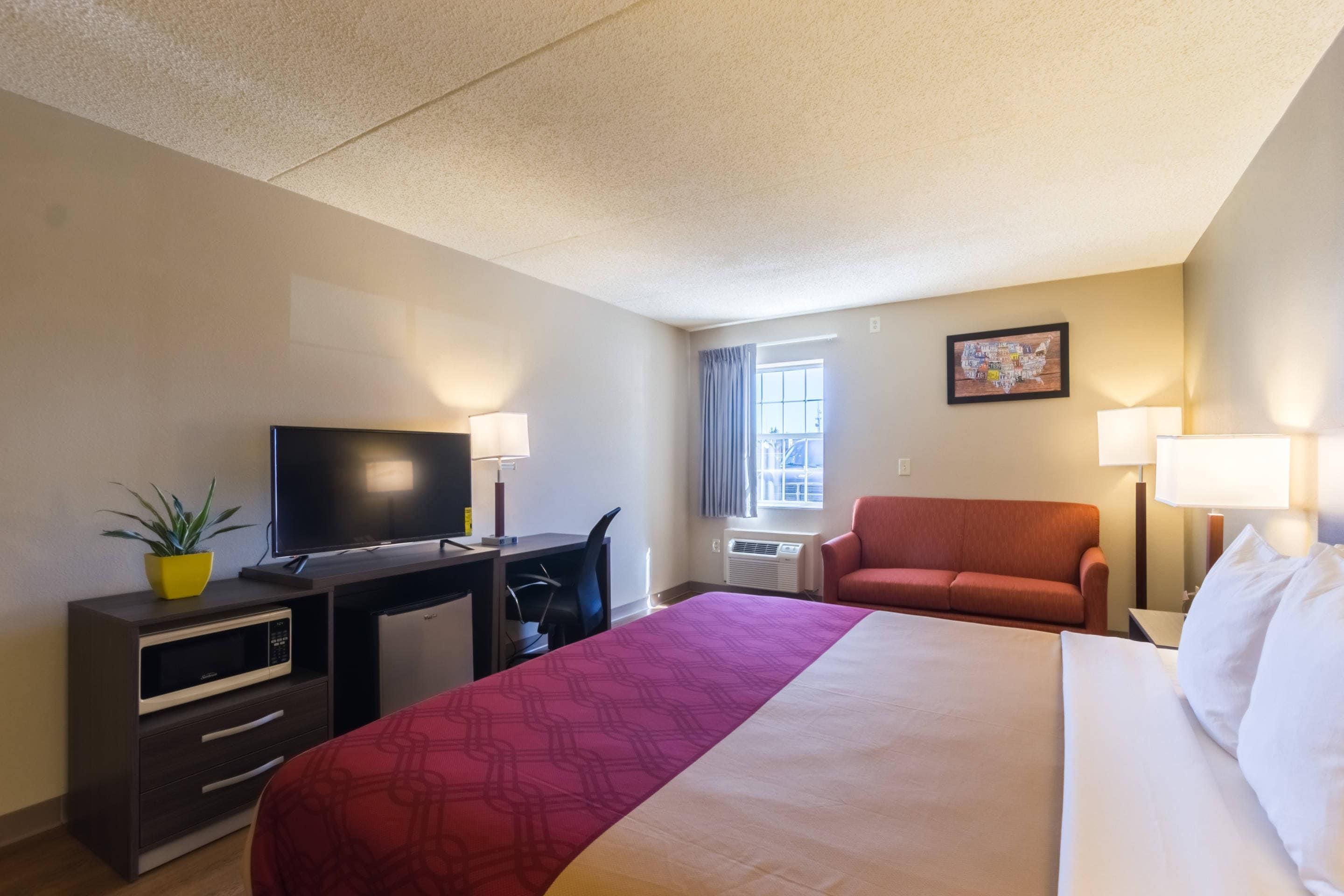 A hotel room with a bed, desk, chair, television, and a window with curtains.