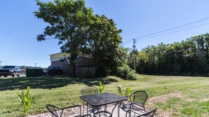 A patio with a table and chairs, surrounded by a grassy lawn and a tree.