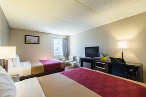 Ein Hotelzimmer mit zwei Betten, einem Schreibtisch mit Fernseher, einem Sessel, einer Schreibtischlampe und einem Fenster mit Vorhängen.