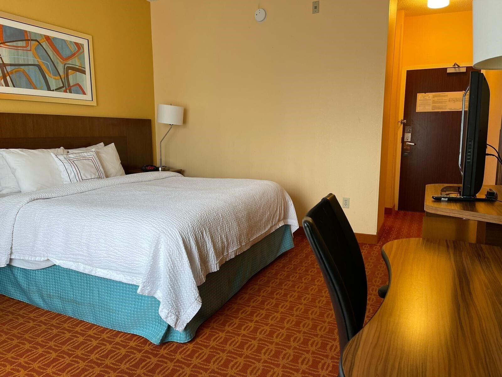 Ein Hotelzimmer mit Bett, Schreibtisch, Stuhl, Lampe und Fernseher.
