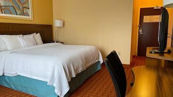 Una habitación de hotel con una cama, un escritorio, una silla, una lámpara y un televisor.