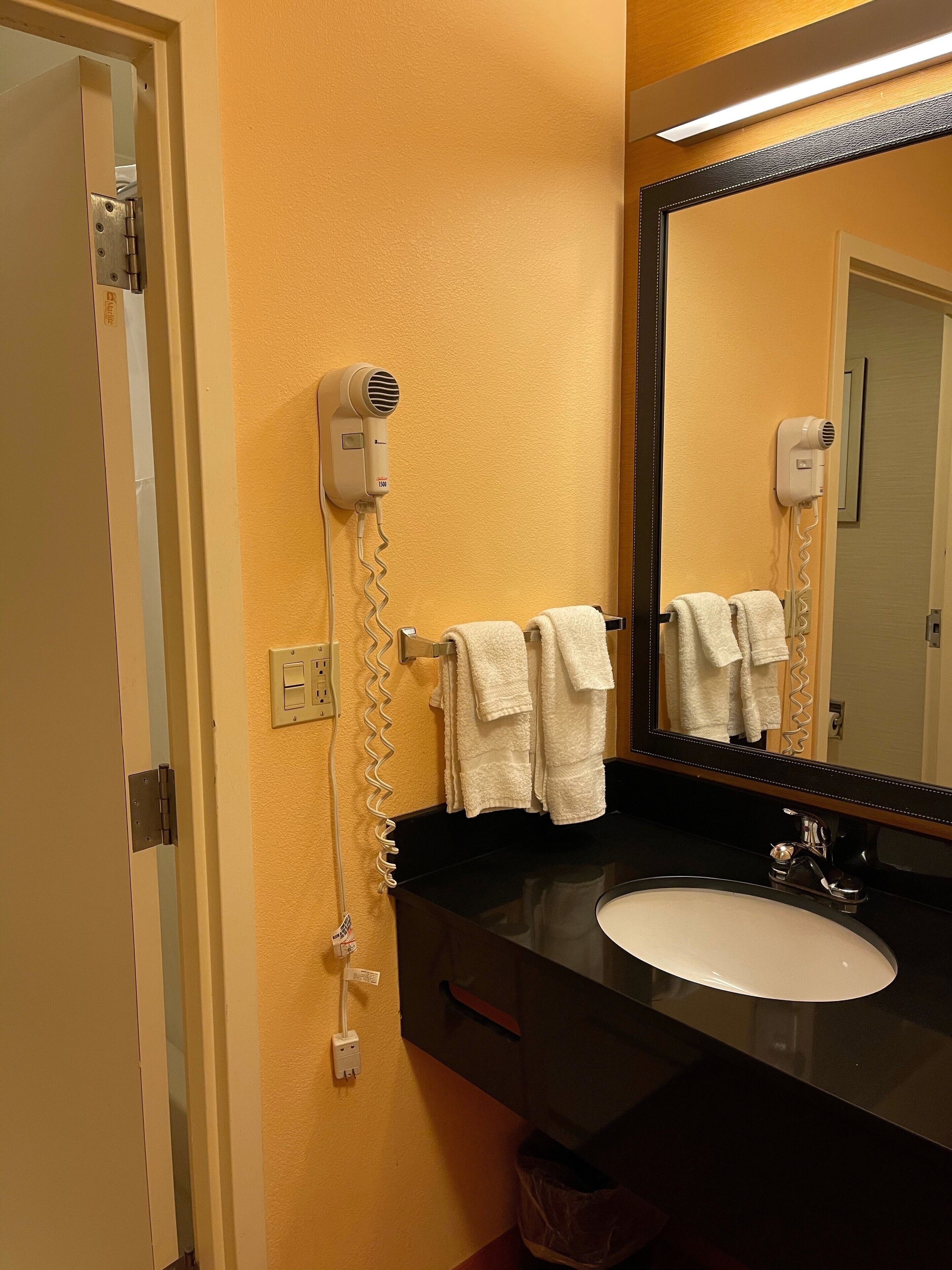 A bathroom with a black sink, a mirror, and two hair dryers mounted on the wall.