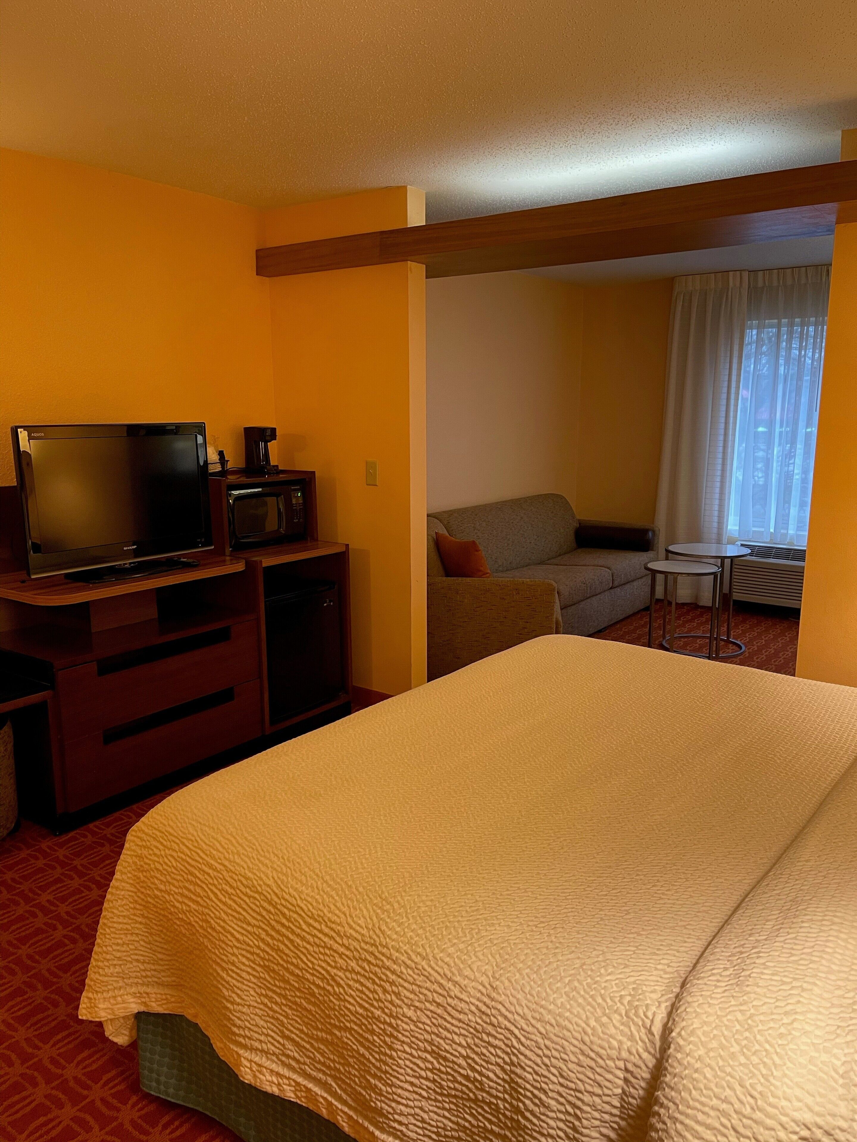 Een hotelkamer met een bed, een televisie, een magnetron, een bank en een klein tafeltje.