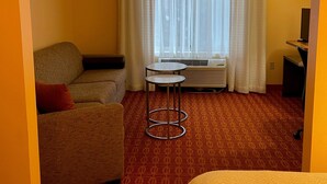 Une chambre d’hôtel avec un canapé, une petite table, un lit, un radiateur et une fenêtre avec des rideaux.