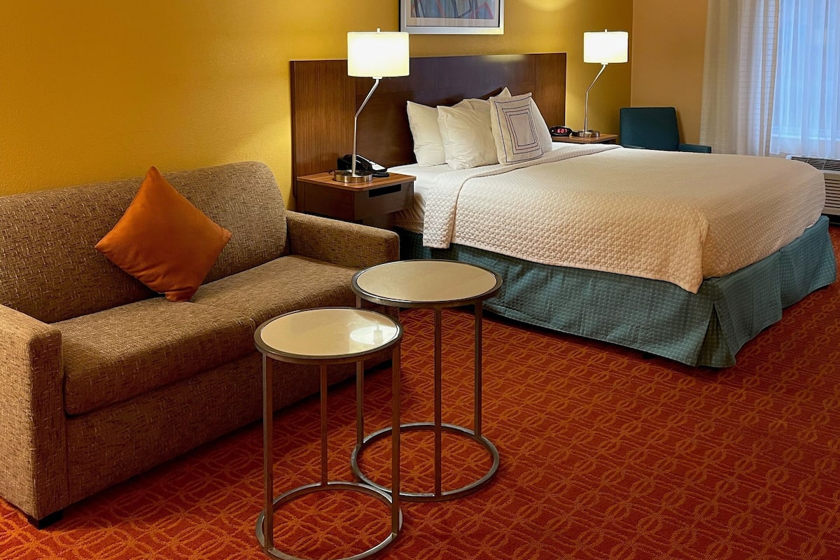 A hotel room with a bed, a sofa, two small tables, and a nightstand.