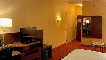 Een hotelkamer met een bed, een bureau met een televisie, een stoel, een lamp en een klein tafeltje.