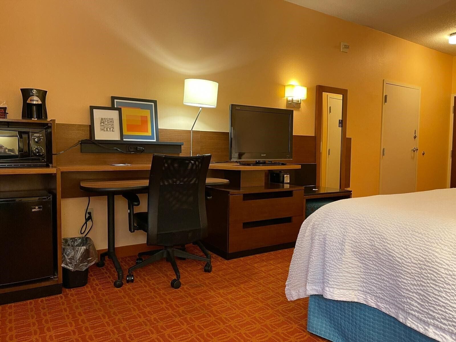A hotel room with a bed, desk, chair, television, microwave, and a trash bin.