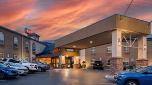 Een hotel met een overdekte ingang, een parkeerplaats met meerdere auto's en een zonsonderganglucht.