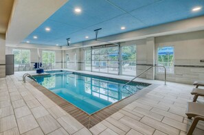 Une piscine intérieure offrant une vue dégagée sur l’extérieur, une chaise de maître-nageur et un escalier pour accéder à la piscine.