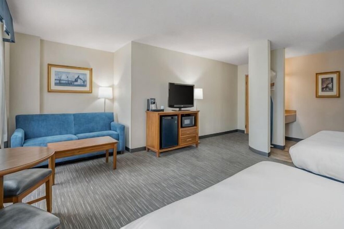 Ein Hotelzimmer mit einem blauen Sofa, einem Fernseher auf einem Holzschrank, einem Schreibtisch und einem Bett.