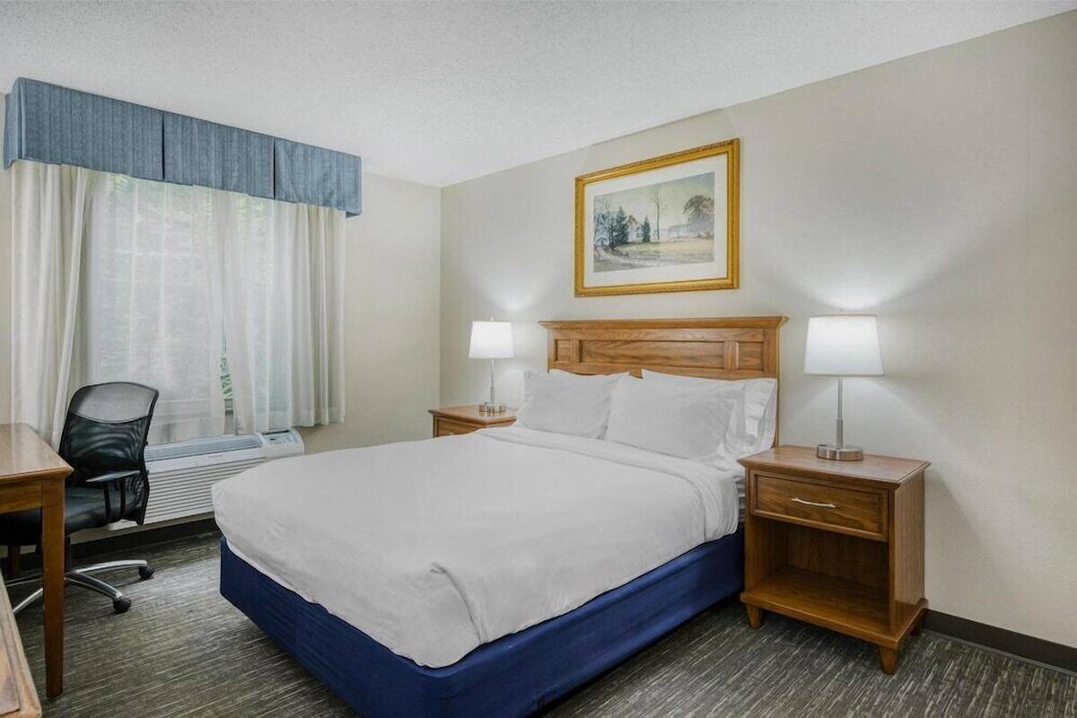 Une chambre d’hôtel comprenant un lit, deux tables de chevet avec des lampes, un bureau, une chaise, un radiateur et un tableau au mur.