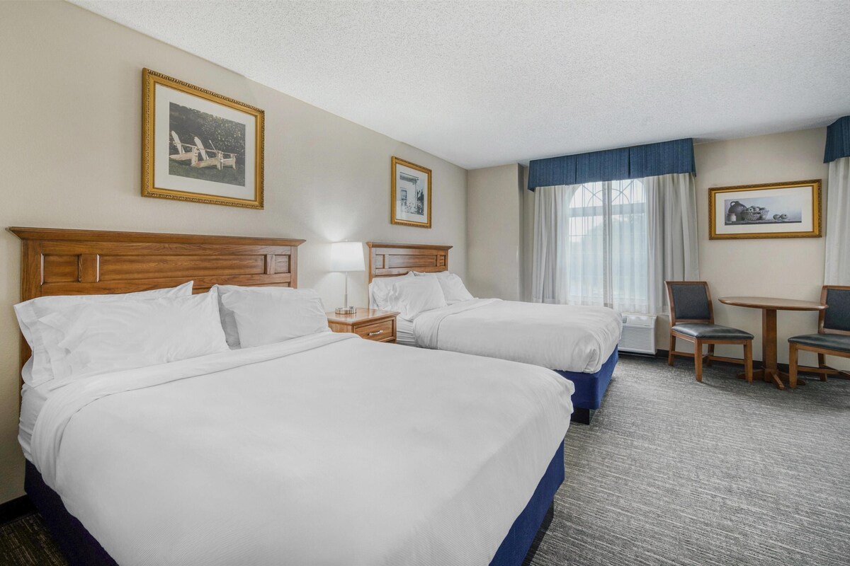 Ein Hotelzimmer mit zwei Betten, einem Schreibtisch, Stühlen und gerahmten Bildern an den Wänden.