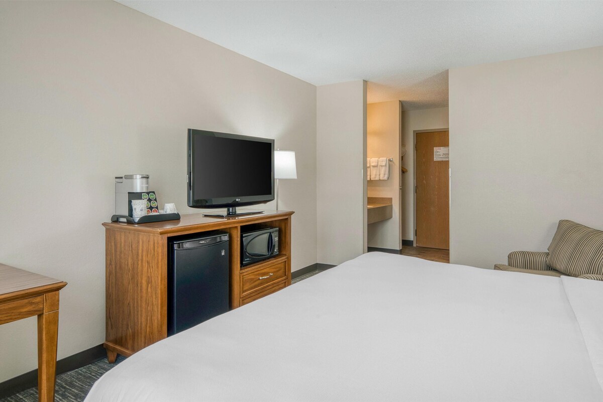 Ein Hotelzimmer mit einem Bett, einem Fernseher auf einem Holzständer, einer Kaffeemaschine, einer Mikrowelle und einer Tür zu einem Badezimmer.