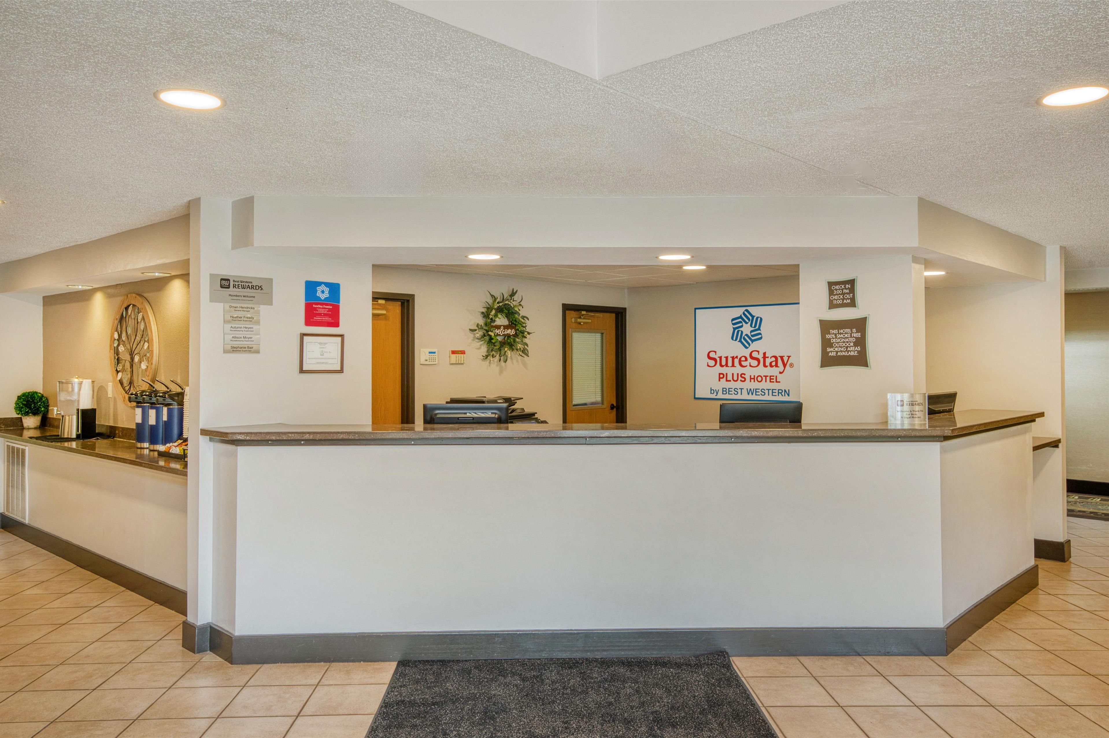 A reception area with a reception desk, a sign for SureStay PLUS HOTEL by BEST WESTERN, and a wall-mounted sign indicating a rewards program.