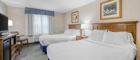 A hotel room with two beds, a desk with a TV, a chair, and a small table.