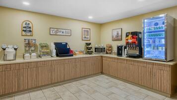 A self-service breakfast area with a coffee bar, microwave, and refrigerated drink dispenser.