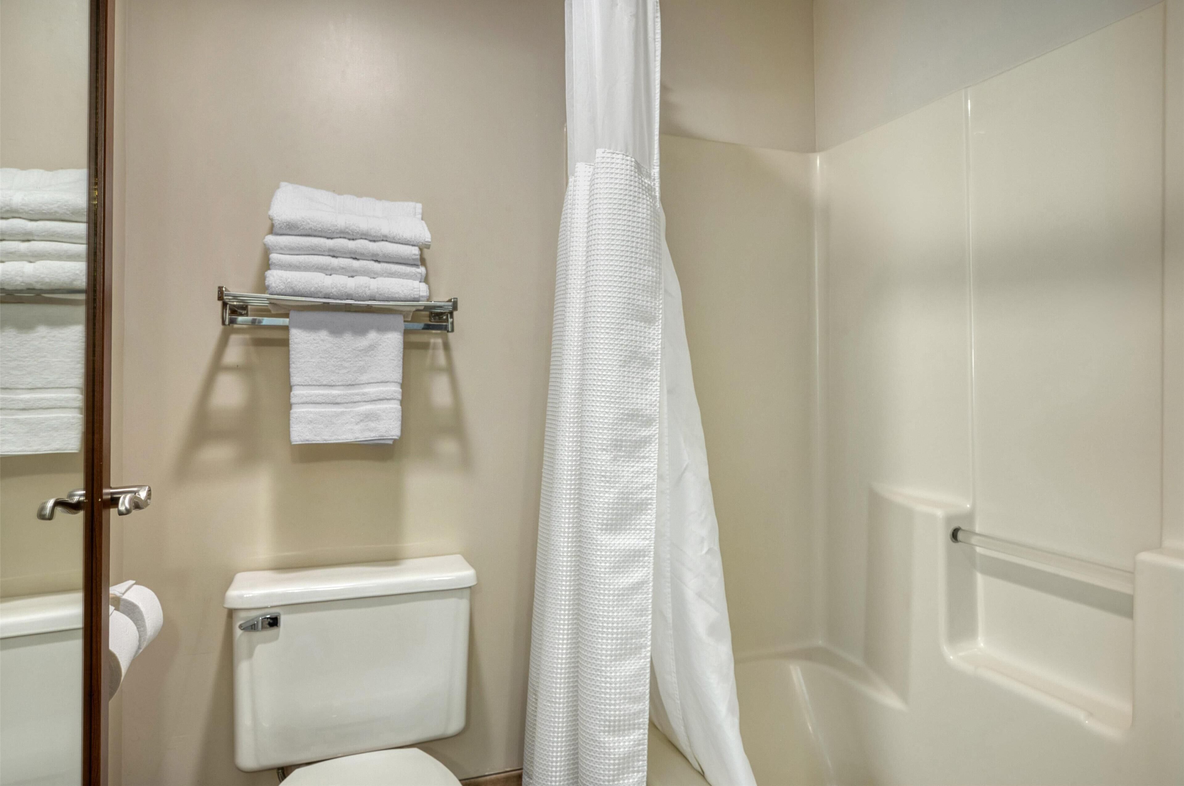 A bathroom with a toilet, a towel rack with folded towels, and a shower curtain.