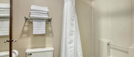 A bathroom with a toilet, a towel rack with folded towels, and a shower curtain.