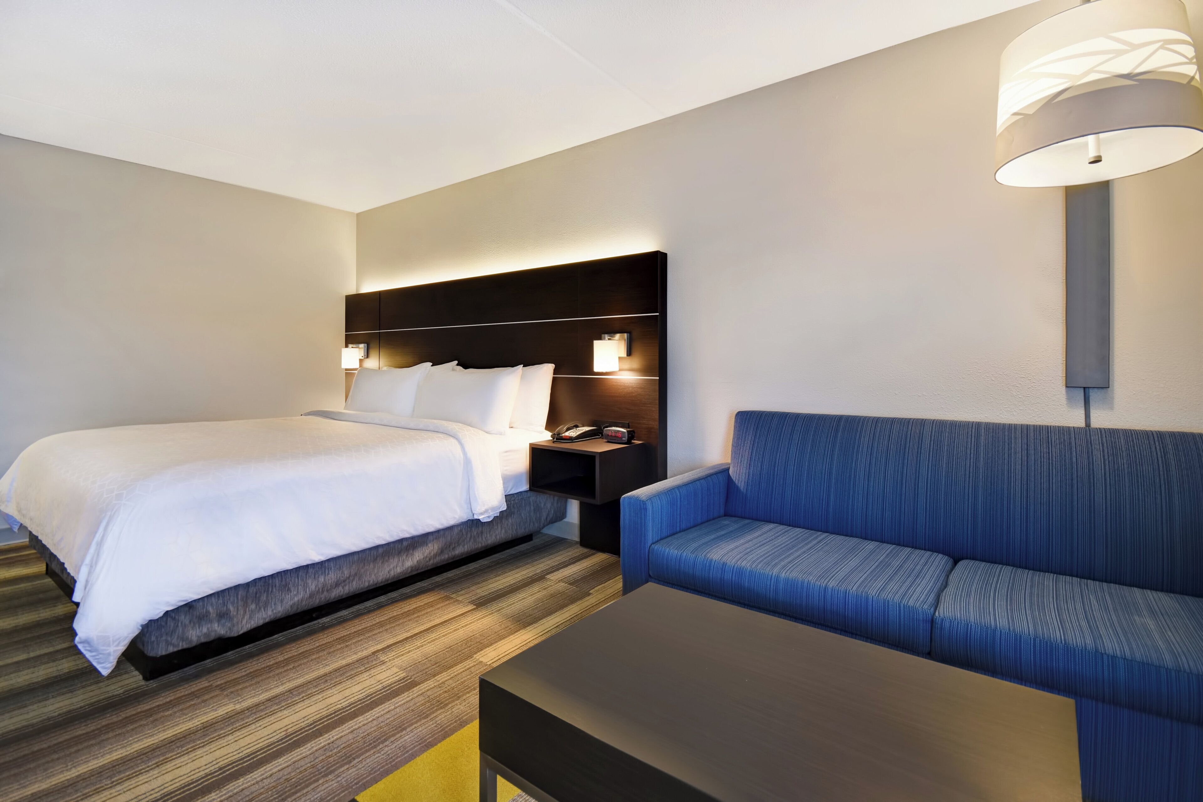 Una habitación de hotel con cama, sofá, mesita de noche y lámpara.