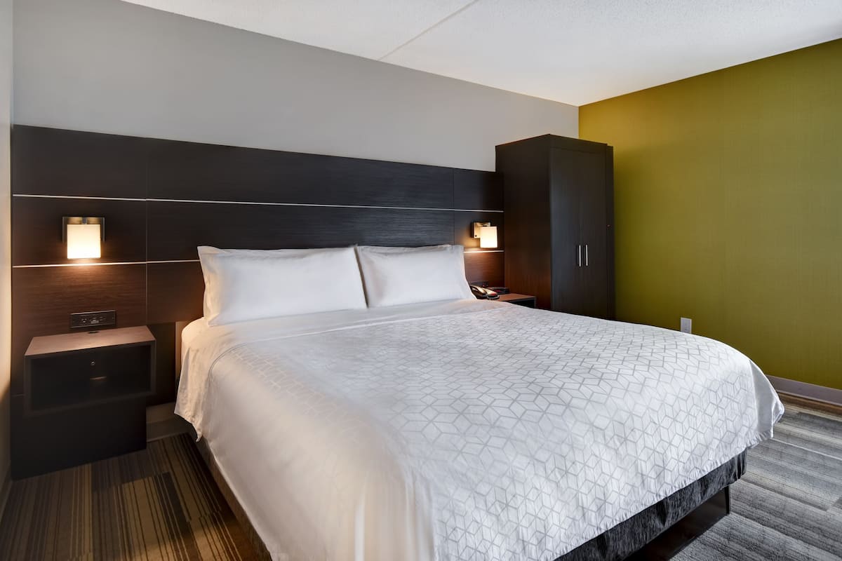 Een hotelkamer met een groot bed, twee nachtkastjes, een kledingkast en wandlampen.