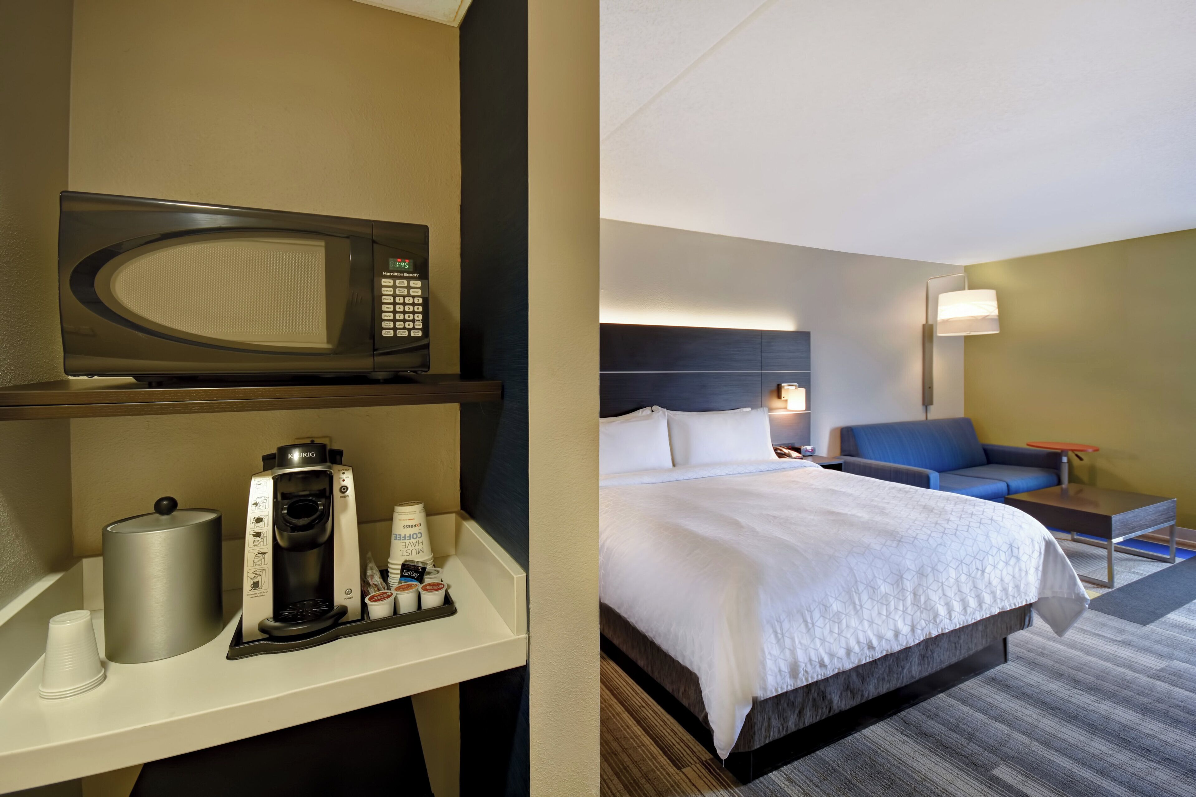 Una habitación de hotel con una cama, zona de estar, microondas y cafetera.
