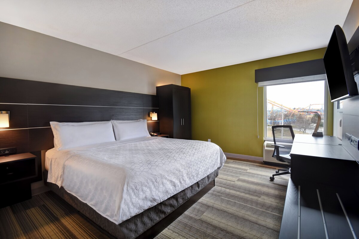 Quarto de hotel com cama, escrivaninha, televisão e janela com vista para um parque de diversões.