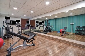 Ein Fitnessraum mit Laufbändern, Crosstrainern, einer Hantelbank und einer Spiegelwand.