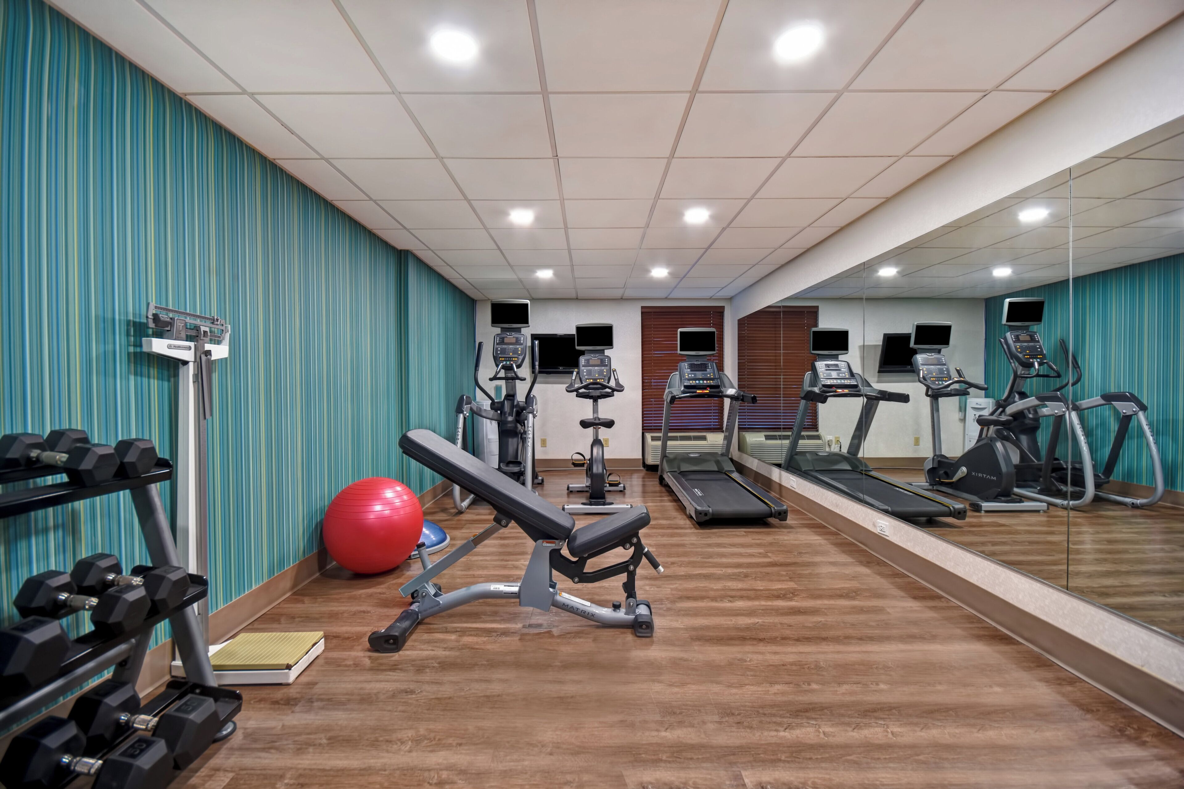 A gym with exercise equipment, a bench, and a red exercise ball.