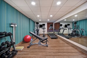 A gym with exercise equipment, a bench, and a red exercise ball.