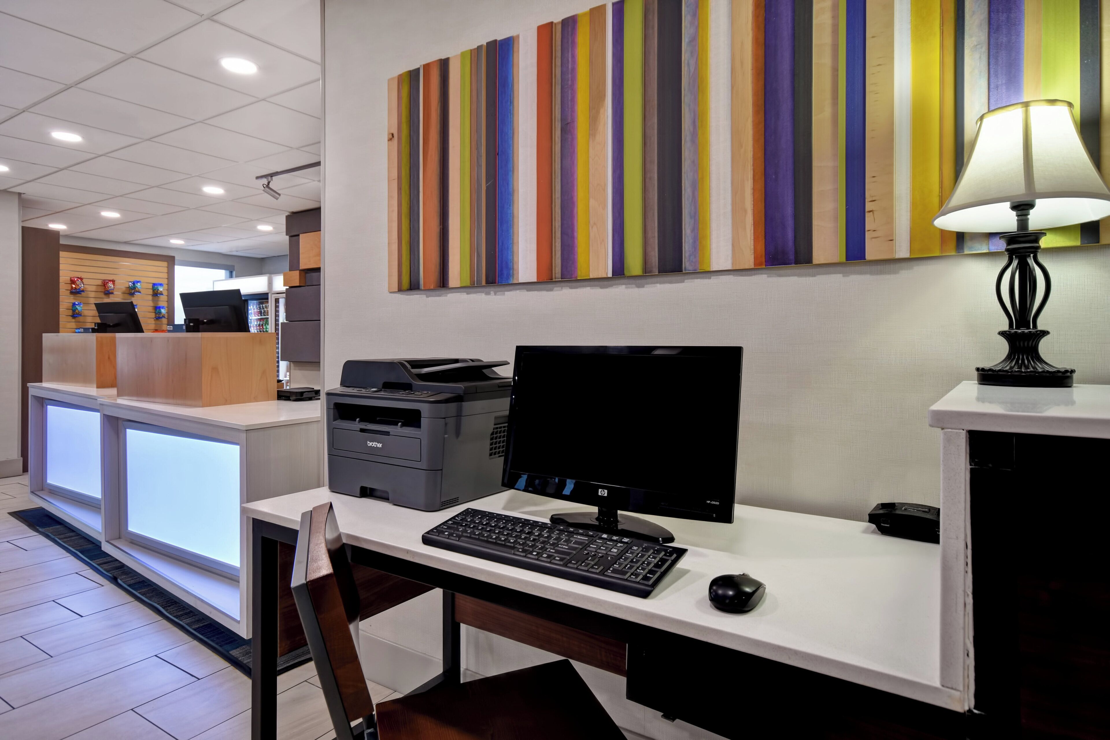 A modern office space with a desk, computer, printer, and a colorful abstract painting on the wall.