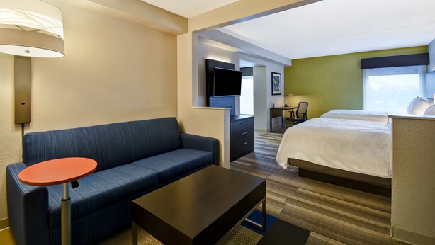 Une chambre d’hôtel avec un canapé, une petite table, un lit, une télévision et un bureau.