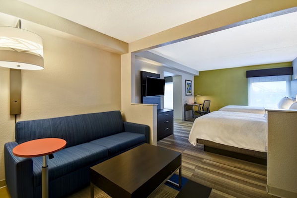 Une chambre d’hôtel avec un canapé, une petite table, un lit, une télévision et un bureau.