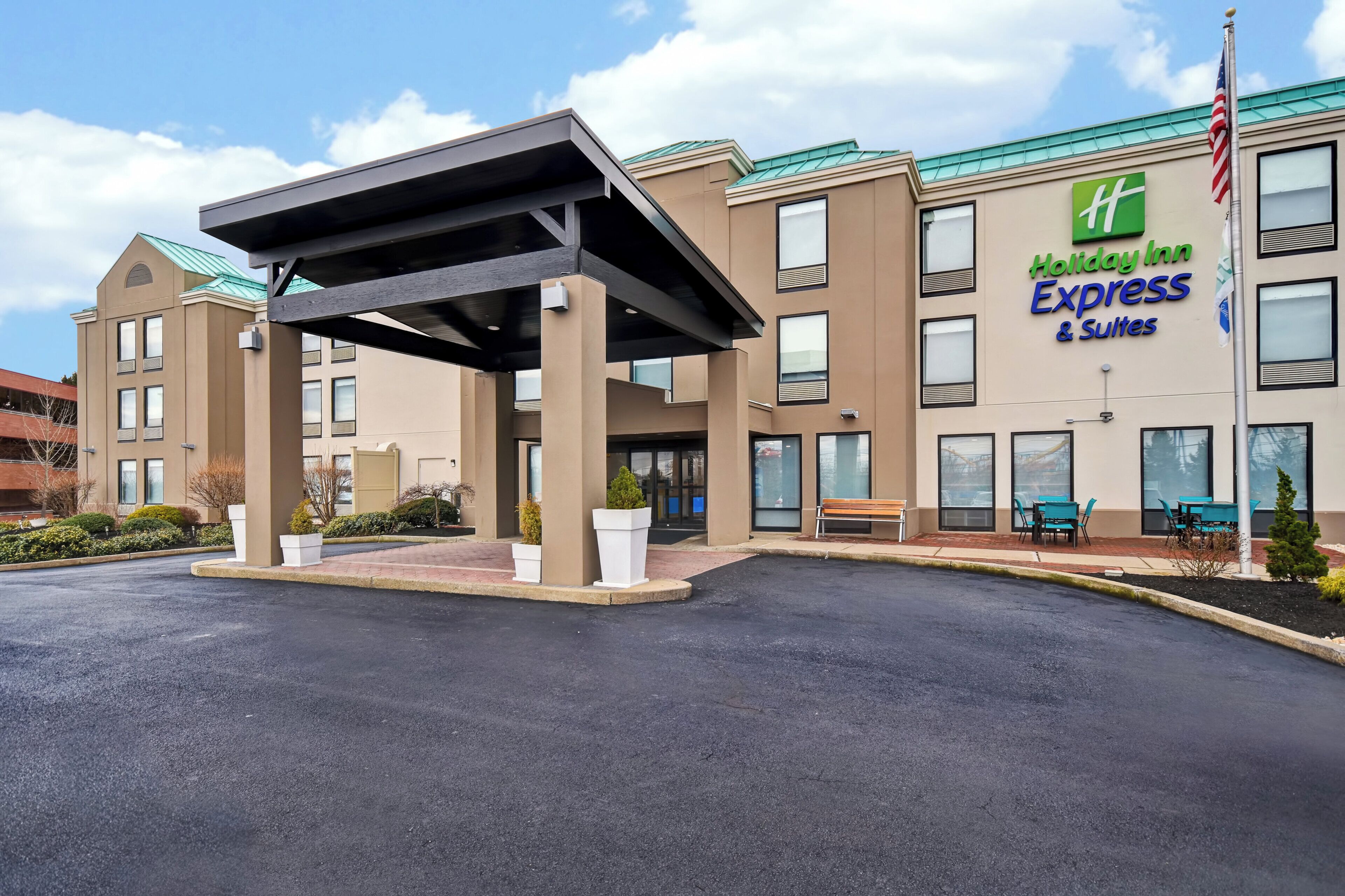 A Holiday Inn Express & Suites building with a covered entrance, outdoor seating, and a flag.