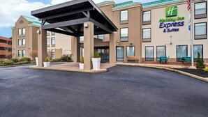A Holiday Inn Express & Suites building with a covered entrance, outdoor seating, and a flag.