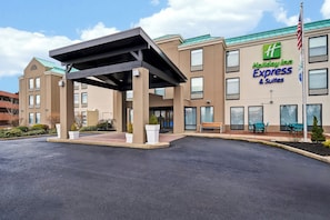 A Holiday Inn Express & Suites building with a covered entrance, outdoor seating, and a flag.