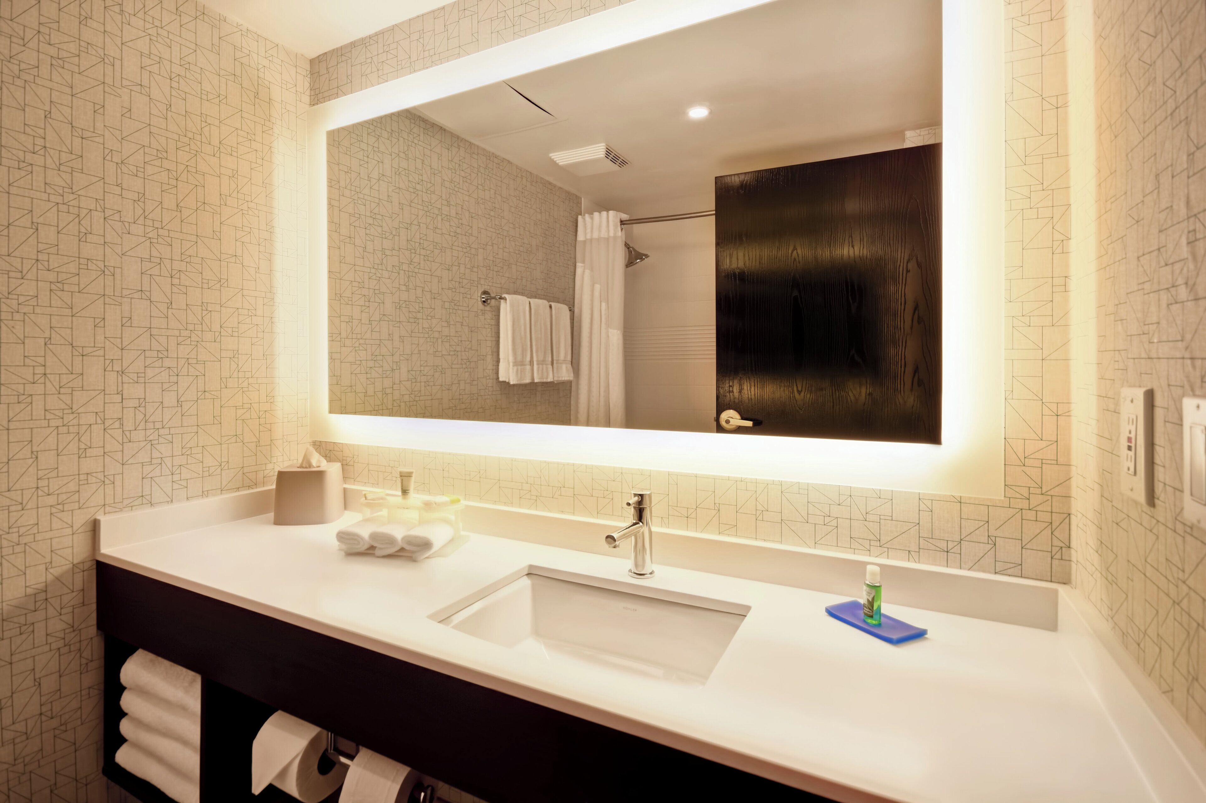 A modern bathroom with a large mirror, two sinks, and a towel rack.