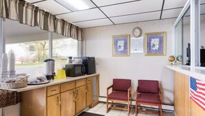 A small kitchenette with a microwave, toaster, and coffee maker. There are two red chairs and a small table with a basket and a plate. - Royal Inn Clearfield (Clearfield)