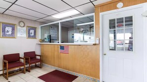 A reception area with a wooden counter, two red chairs, a tiled floor, and a white door. - Royal Inn Clearfield (Clearfield)