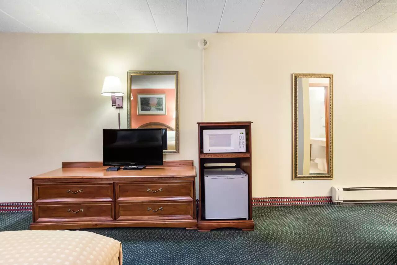 Une chambre d’hôtel équipée d’une commode en bois, d’un téléviseur à écran plat, d’un four à micro-ondes, d’un réfrigérateur, d’un lit, d’une lampe et d’un miroir.