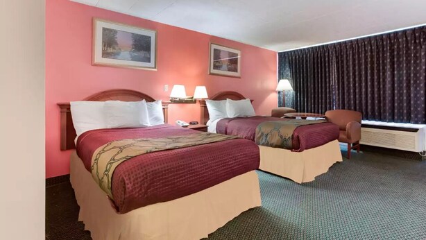 A hotel room with two beds, a desk, a chair, and a window with curtains. - Royal Inn Clearfield (Clearfield)