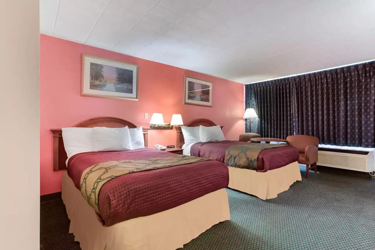 A hotel room with two beds, a desk, a chair, and a window with curtains.