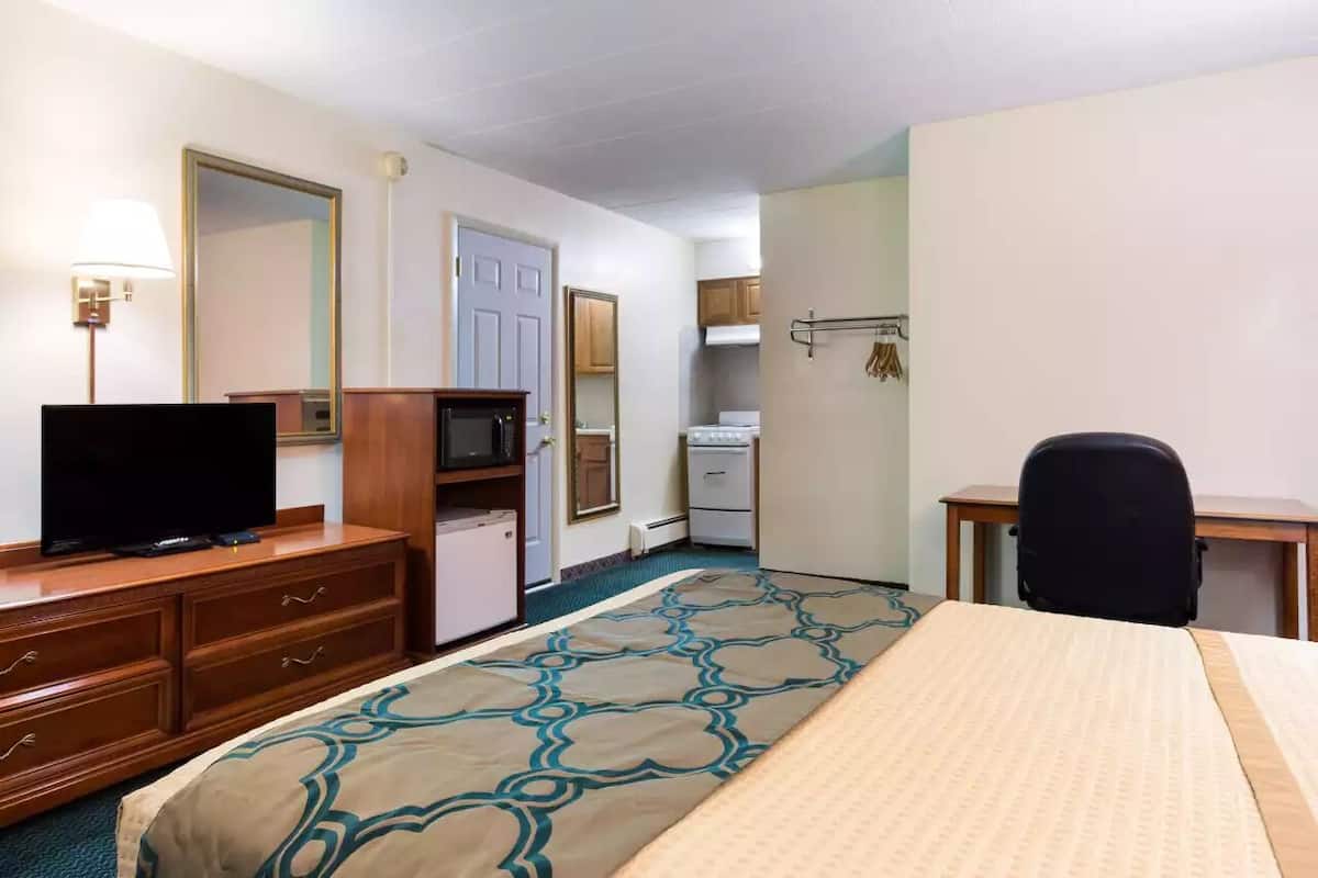 A hotel room with a bed, a desk, a chair, a television, a microwave, a refrigerator, and a bathroom.