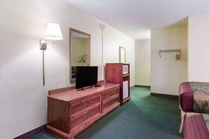 Quarto de hotel com cama, televisão sobre uma cômoda de madeira, espelho, luminária e cabideiro.