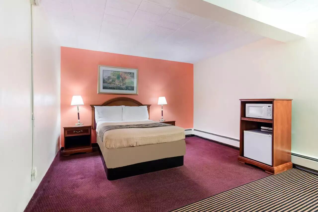 Een hotelkamer met een bed, twee bedlampen, een nachtkastje, een houten kast en een schilderij aan de muur.